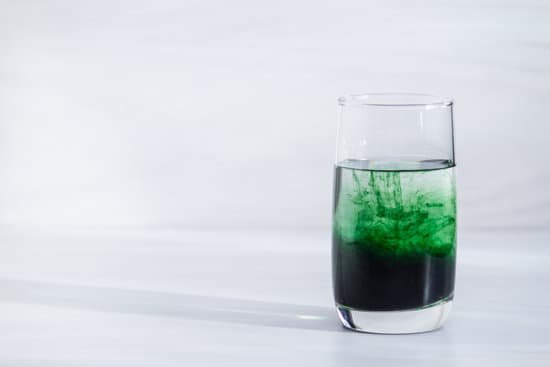 canva chlorophyll in glass of water on white wooden background. copy space sunlight.