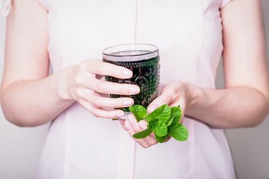 canva female hand holding glass of green chlorophyll drink with mint leaves on a light pink background MAEA Qg4noc