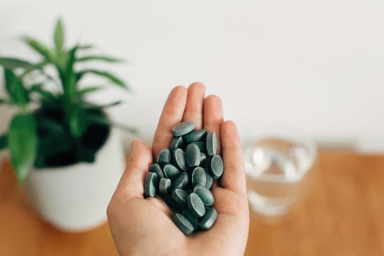 canva hand holding chlorophyll tablets above glass of water on wooden MAEYTYTrK9s