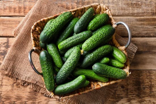 canva many green fresh cucumbers in wicker basket on wooden table