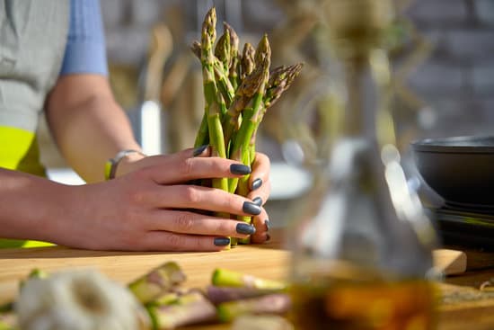 canva woman holding a bunch of green asparagus in the kitchen MAEAGr7HlKY