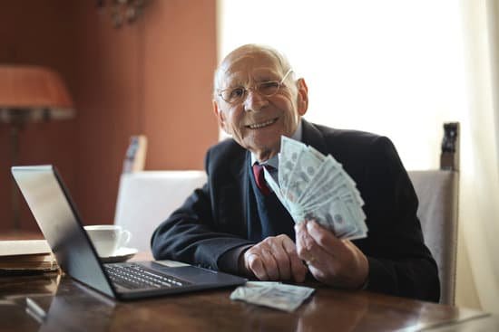 canva happy senior businessman holding money in hand while working on laptop at table MAD7JTNhOUM
