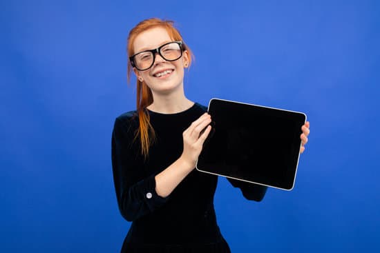 canva smart serious red haired teenager girl in glasses holds a tablet with a blank screen mock up to insert a page on a blue background MAEUrjQj9w0