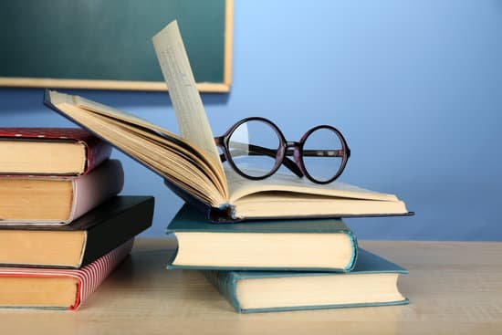 canva stack of books with glasses on wooden desk MAD MBaErvg