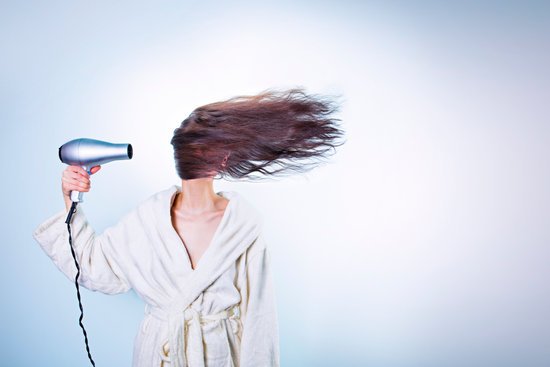 canva woman holding gray hair dryer and wearing white bathrobe