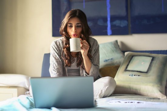 canva woman in grey jacket sits on bed uses grey laptop MADGyRA93wg